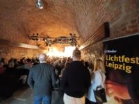 Gefüllter Veranstaltungsraum in den Gemäuern der Moritzbastei. Menschen sitzen auf Stühlen, weitere Menschen stehen und lauschen dem Podium auf der Bühne.