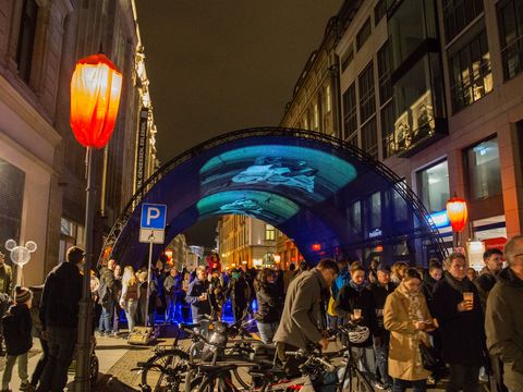 Im Vordergrund sieht man viele Menschen und eine orange leuchtende Laterne, im Hintergrund ist ein Tunnel mit Lichtprojektionen zu sehen