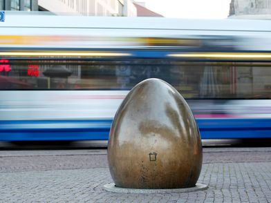 Demokratieglocke vor einer verschwommenen fahrenden Straßenbahn