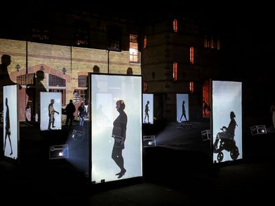 Große LED-Screens, auf denen die Umrisse und Schatten von Menschen in Bewegung zu sehen sind