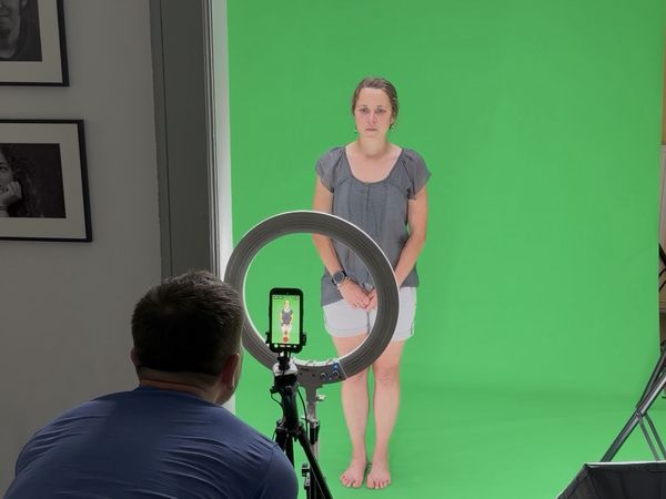 Eine Frau steht für Videoaufnahmen vor einem grünen Hintergrund